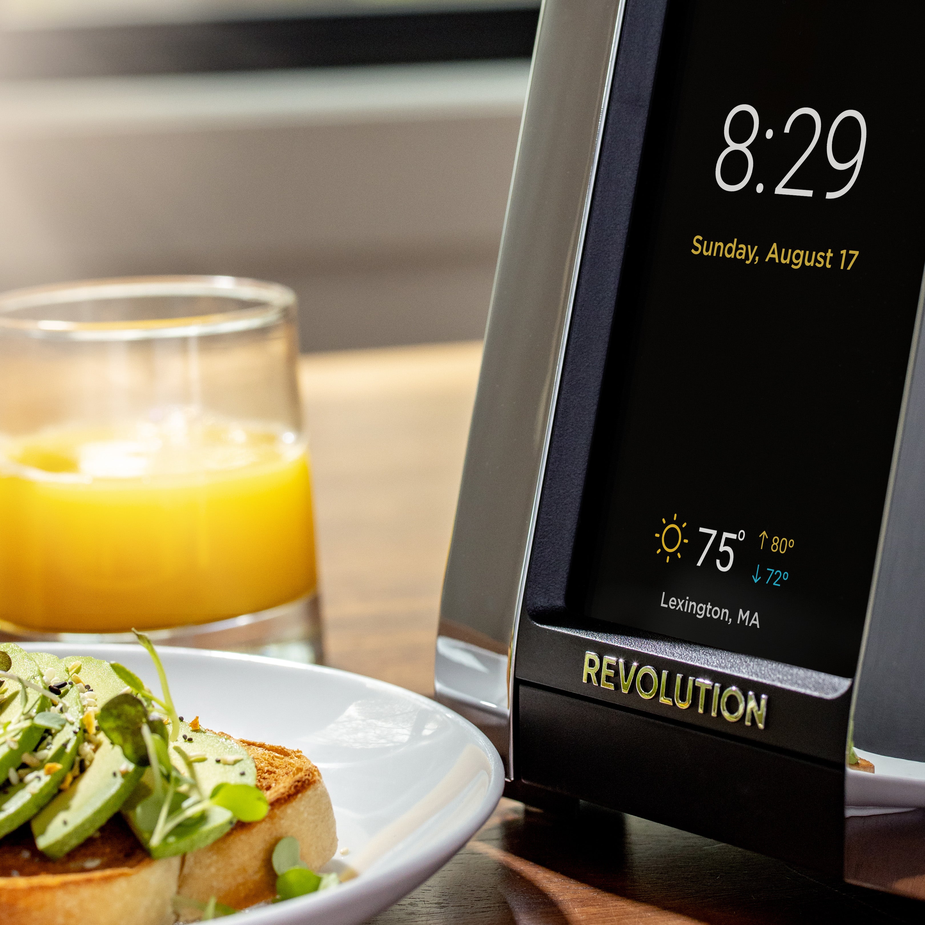 A digital clock shows 8:29 and Sunday, August 17, with weather details for Lexington, MA. Nearby are a glass of orange juice and avocado toast. The clock features "R180 Connect Smart Toaster" at the bottom by Revolution Cooking, highlighting its InstaGLO® Heating Technology.